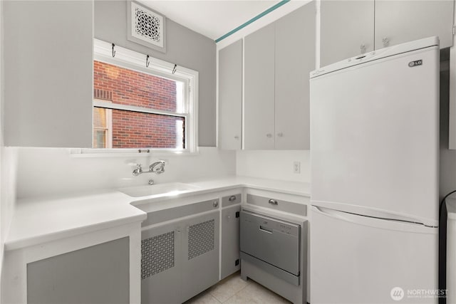 kitchen featuring light countertops, visible vents, freestanding refrigerator, a sink, and dishwashing machine