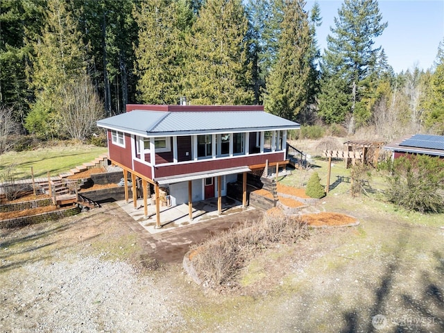 view of front facade featuring metal roof, driveway, a deck, and a view of trees