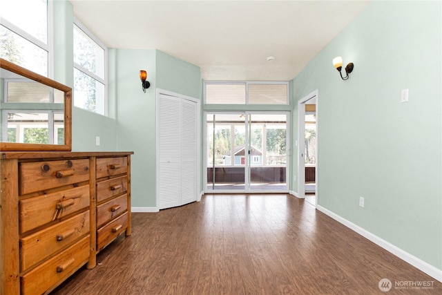 unfurnished bedroom featuring access to exterior, multiple windows, baseboards, and dark wood-style floors