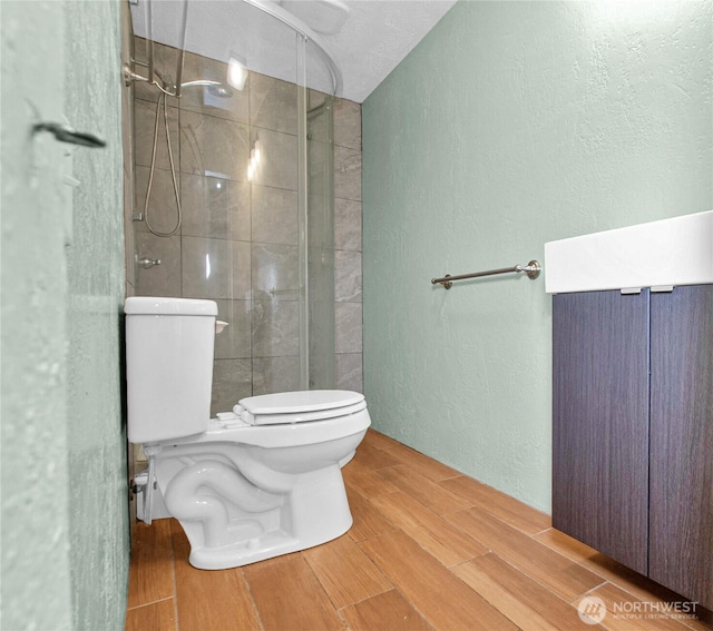 bathroom with a textured wall, wood finish floors, toilet, and a stall shower