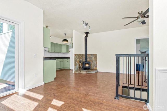 unfurnished living room with a wood stove, baseboards, a ceiling fan, and wood finished floors