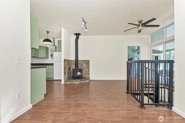 interior space featuring ceiling fan, wood finished floors, a wood stove, and baseboards