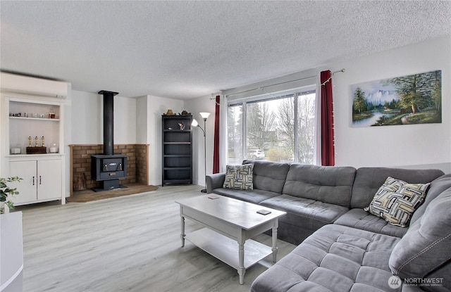 living room with a wall unit AC, a wood stove, wood finished floors, and a textured ceiling