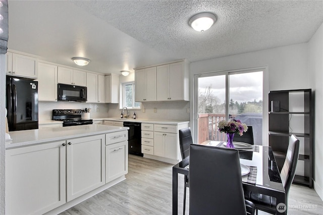 kitchen featuring light wood-style flooring, black appliances, light countertops, and a sink