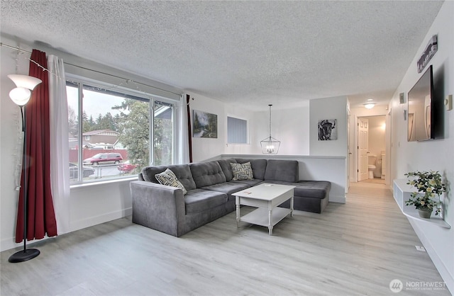 living room with an inviting chandelier, wood finished floors, baseboards, and a textured ceiling