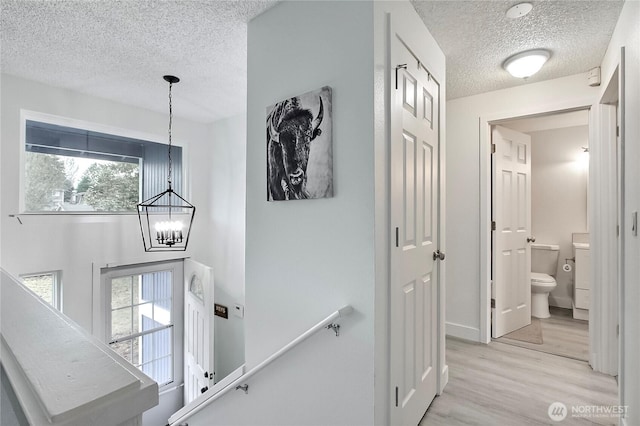 hallway with light wood-type flooring, an upstairs landing, a notable chandelier, and a textured ceiling