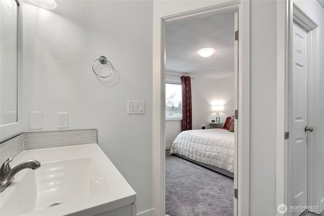 bathroom featuring ensuite bath, a textured ceiling, and a sink