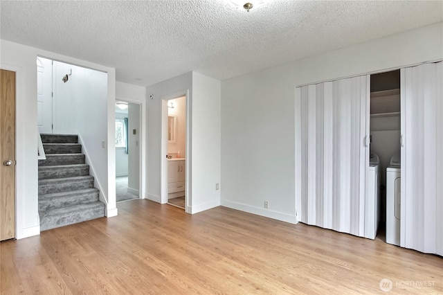 unfurnished living room with light wood-style flooring, a textured ceiling, baseboards, stairs, and washing machine and clothes dryer