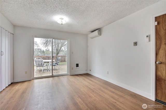 unfurnished room with a textured ceiling, a wall mounted air conditioner, baseboards, and wood finished floors