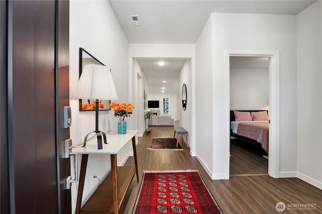 hall with dark wood-style floors, visible vents, and baseboards