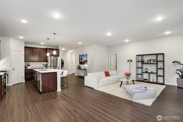 kitchen with dark wood-type flooring, freestanding refrigerator, open floor plan, dark brown cabinets, and a kitchen breakfast bar