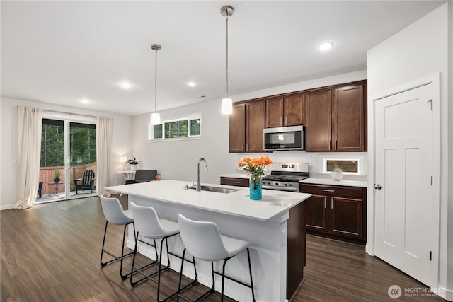 kitchen with a breakfast bar, dark wood-style flooring, light countertops, appliances with stainless steel finishes, and a sink