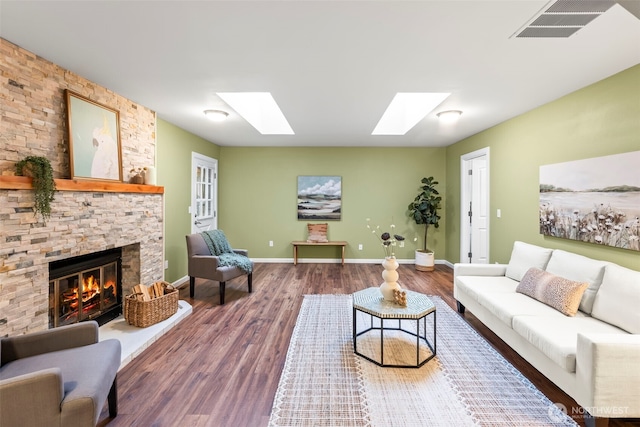 living room featuring a stone fireplace, a skylight, wood finished floors, visible vents, and baseboards