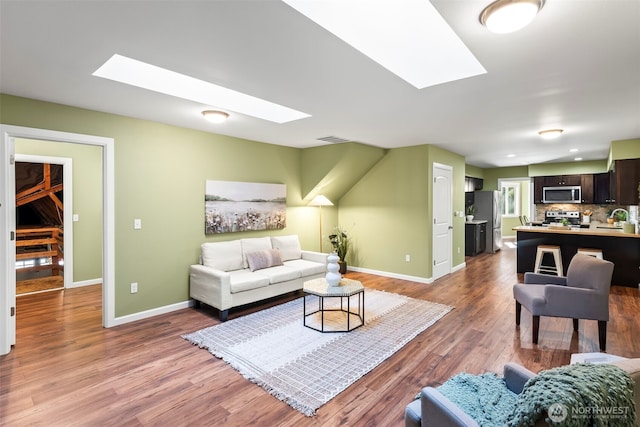 living room with a skylight, visible vents, baseboards, and wood finished floors