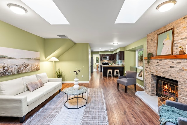 living area featuring a skylight, visible vents, a stone fireplace, wood finished floors, and baseboards