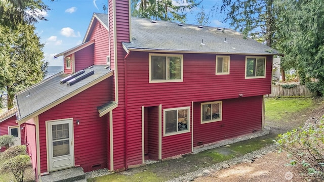 rear view of property featuring crawl space, a chimney, fence, and roof with shingles