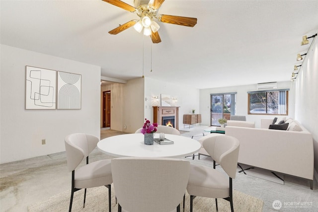 dining room featuring a warm lit fireplace, a wall unit AC, and a ceiling fan