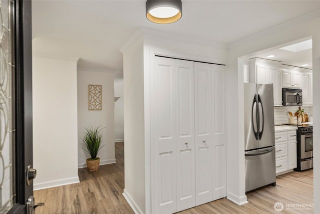 kitchen featuring stainless steel appliances, light wood finished floors, crown molding, and white cabinetry