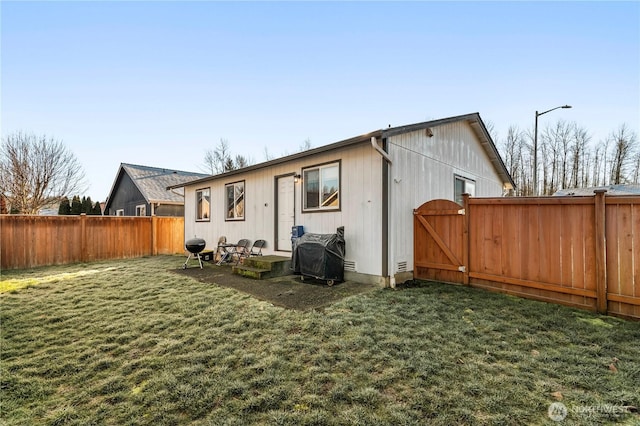 back of house with a lawn, a fenced backyard, and a gate