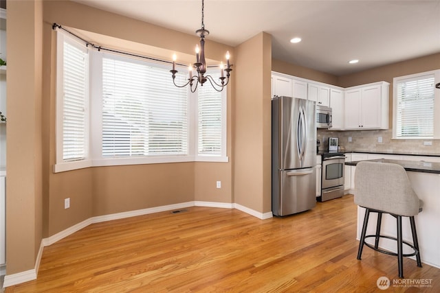 kitchen with white cabinets, light wood-type flooring, stainless steel appliances, and backsplash