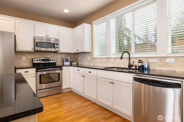 kitchen with light wood-style flooring, stainless steel appliances, a sink, white cabinets, and tasteful backsplash