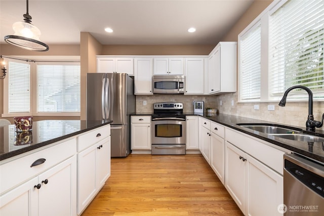 kitchen with appliances with stainless steel finishes, light wood-type flooring, white cabinets, and a sink