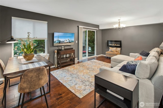 living area with a wealth of natural light, baseboards, wood finished floors, and an inviting chandelier