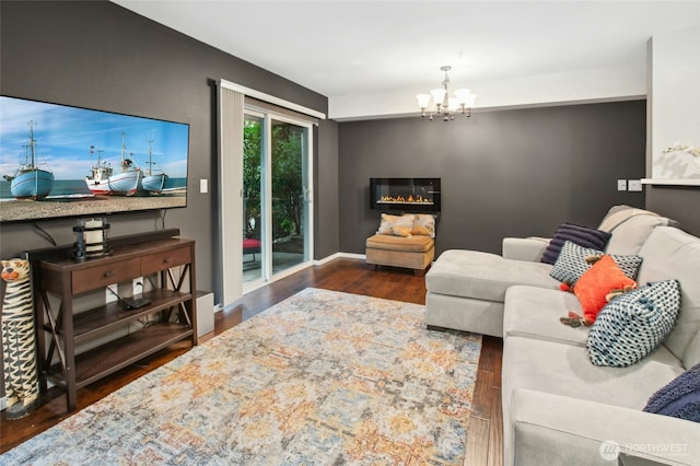 living room with baseboards, a glass covered fireplace, wood finished floors, and a notable chandelier