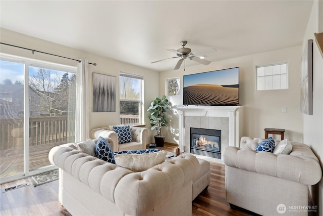 living room with ceiling fan, dark wood-type flooring, a tiled fireplace, and visible vents