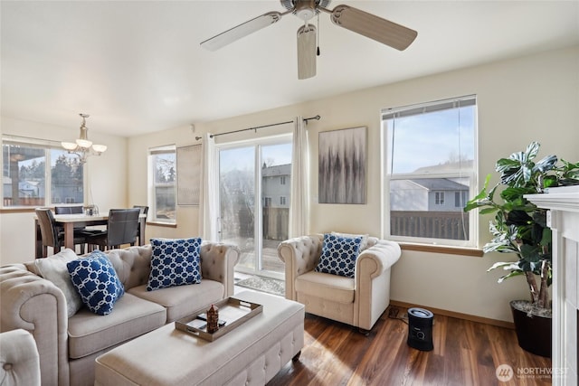 living room with ceiling fan with notable chandelier, a fireplace, wood finished floors, and baseboards