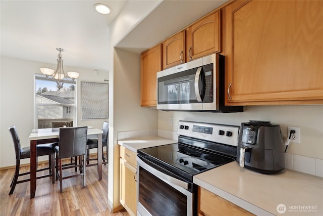 kitchen with light wood-style flooring, light countertops, appliances with stainless steel finishes, hanging light fixtures, and an inviting chandelier