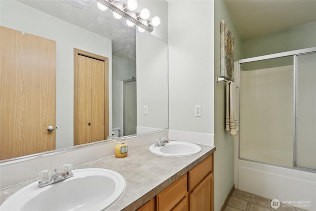 full bath featuring double vanity, combined bath / shower with glass door, and a sink