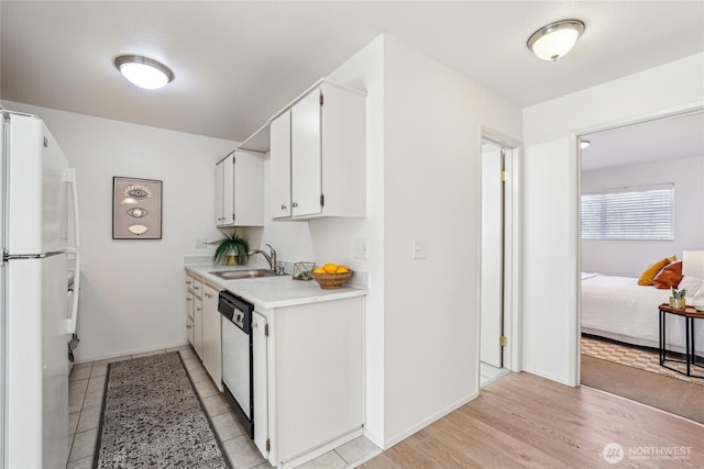 kitchen featuring white cabinets, dishwashing machine, freestanding refrigerator, light countertops, and a sink