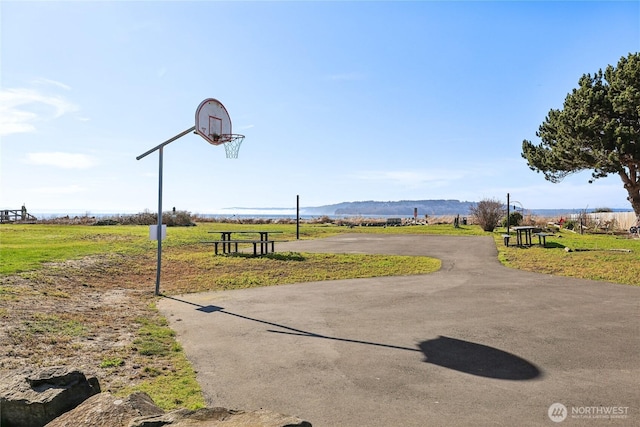 view of community with aphalt driveway, a rural view, community basketball court, and a lawn