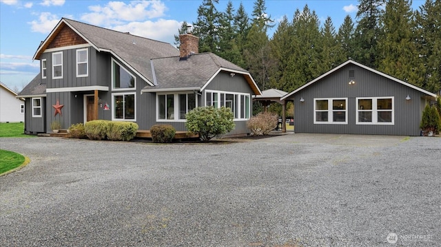 rustic home with roof with shingles, driveway, and a chimney