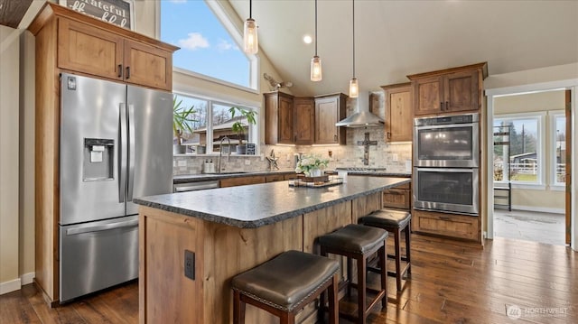 kitchen featuring dark countertops, appliances with stainless steel finishes, a sink, wall chimney range hood, and backsplash