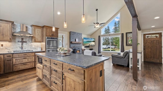 kitchen featuring dark wood-style flooring, stainless steel appliances, dark countertops, decorative backsplash, and wall chimney range hood