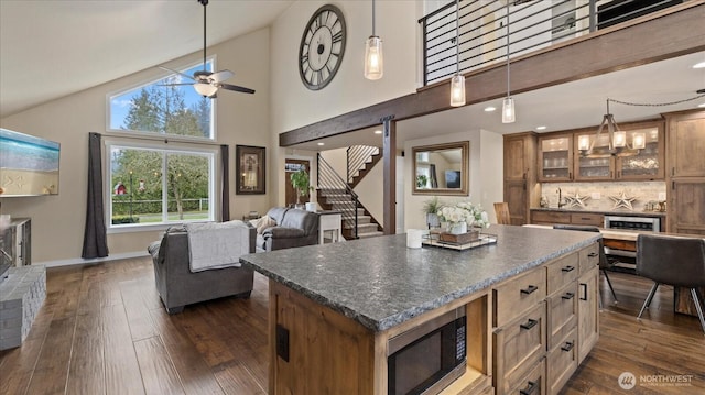 kitchen with dark countertops, stainless steel microwave, dark wood finished floors, and open floor plan