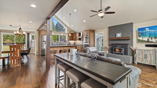 dining area with high vaulted ceiling, ceiling fan with notable chandelier, a fireplace, beam ceiling, and dark wood finished floors