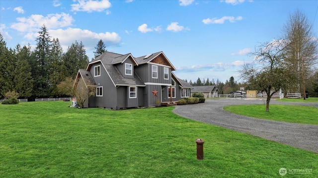 view of front facade featuring a shingled roof, aphalt driveway, fence, board and batten siding, and a front yard