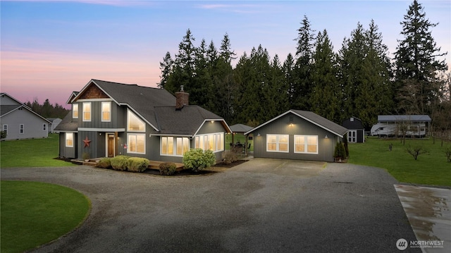 view of front of home featuring gravel driveway, a shingled roof, a chimney, and a lawn