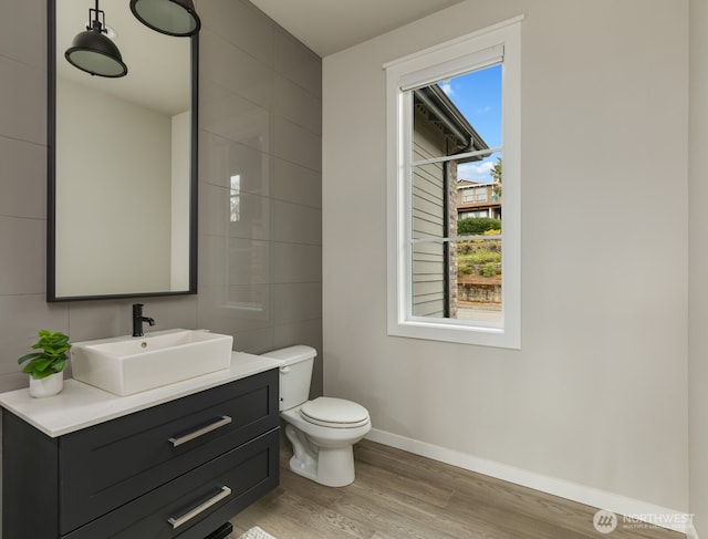 bathroom with toilet, wood finished floors, vanity, tile walls, and baseboards