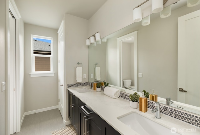 full bath with double vanity, baseboards, toilet, and a sink