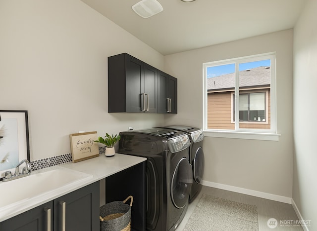 clothes washing area with cabinet space, washing machine and dryer, baseboards, and a sink