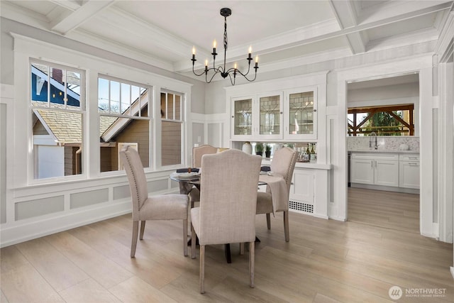 dining area with light wood finished floors, a decorative wall, an inviting chandelier, coffered ceiling, and beamed ceiling