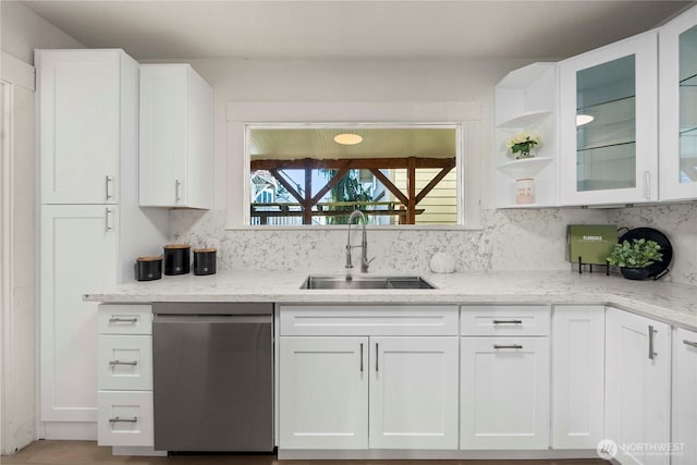 kitchen with decorative backsplash, stainless steel dishwasher, white cabinetry, a sink, and light stone countertops