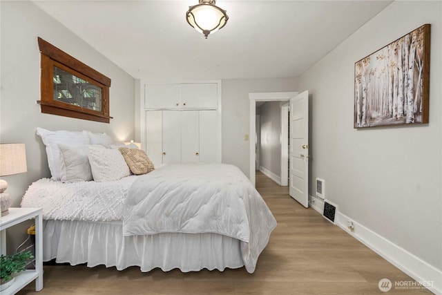 bedroom with light wood finished floors, visible vents, baseboards, and a closet