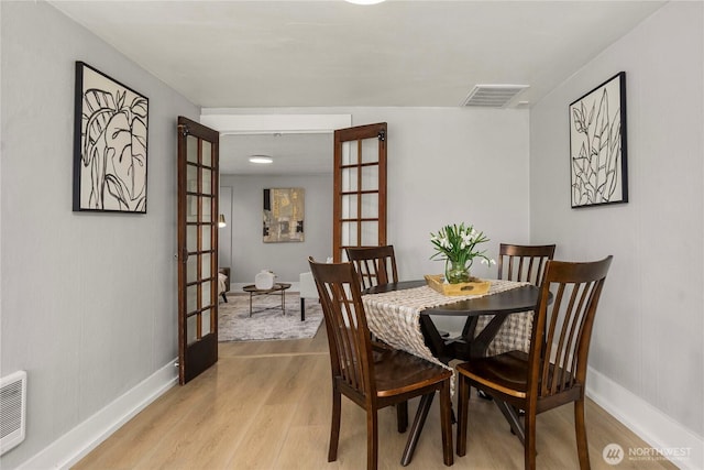 dining area with light wood finished floors, french doors, visible vents, and baseboards