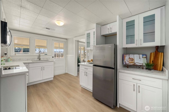 kitchen with a sink, white cabinets, appliances with stainless steel finishes, light wood-type flooring, and glass insert cabinets