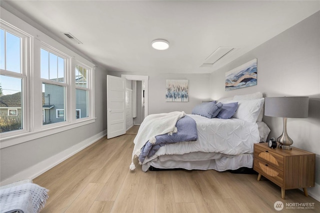 bedroom with light wood-type flooring, attic access, visible vents, and baseboards